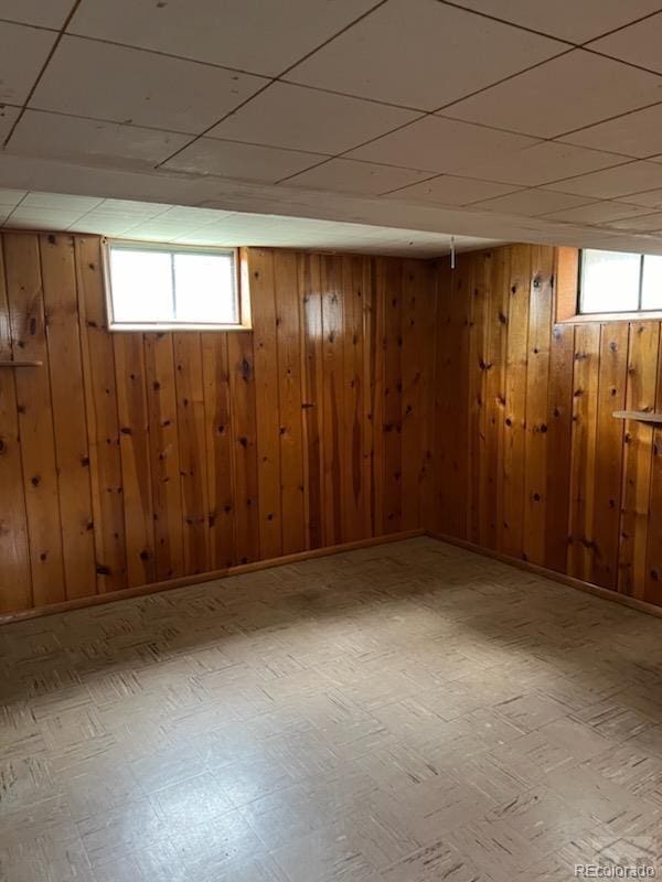 basement with a paneled ceiling and wooden walls