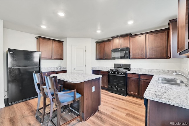 kitchen with light wood-type flooring, a breakfast bar, sink, black appliances, and a center island