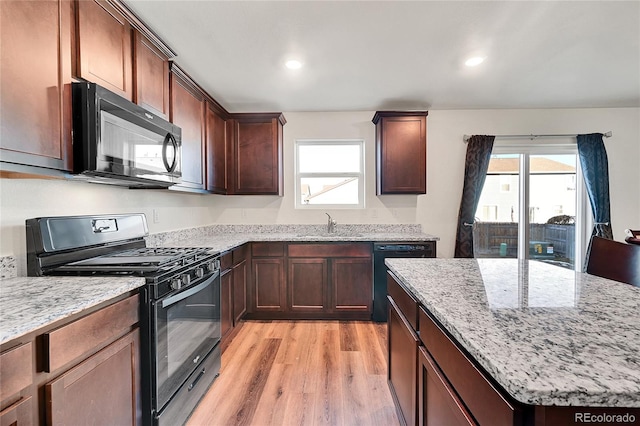 kitchen featuring light stone countertops, light hardwood / wood-style floors, plenty of natural light, and black appliances