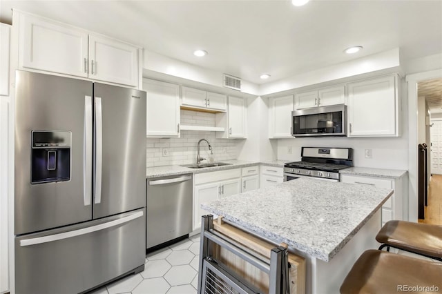 kitchen with appliances with stainless steel finishes, white cabinetry, sink, a breakfast bar area, and light stone countertops