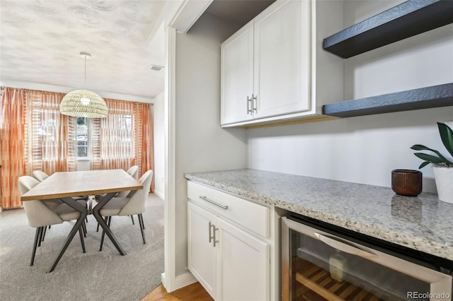 kitchen with wine cooler, pendant lighting, light stone counters, and white cabinets