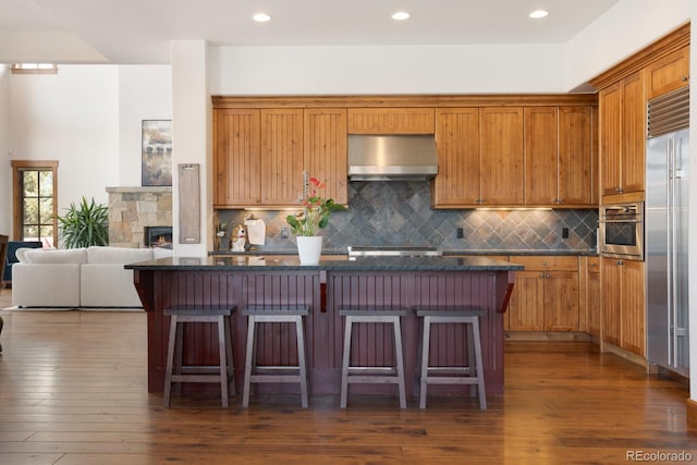 kitchen featuring wall chimney exhaust hood, a kitchen breakfast bar, dark wood-type flooring, and stainless steel appliances