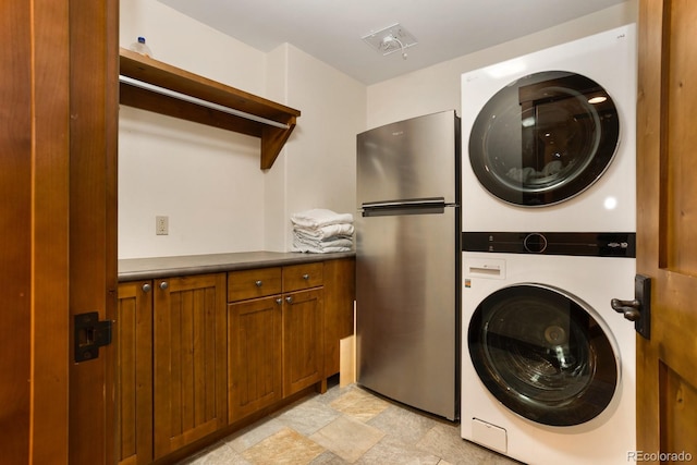 clothes washing area with cabinet space, stacked washer / drying machine, and stone finish flooring