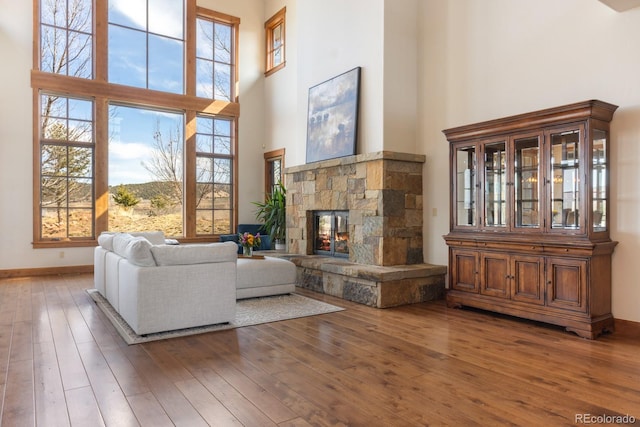 living room featuring baseboards, a fireplace, a towering ceiling, and wood-type flooring