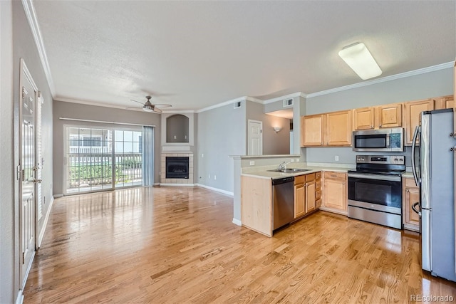 kitchen featuring ceiling fan, a tiled fireplace, light hardwood / wood-style flooring, and stainless steel appliances