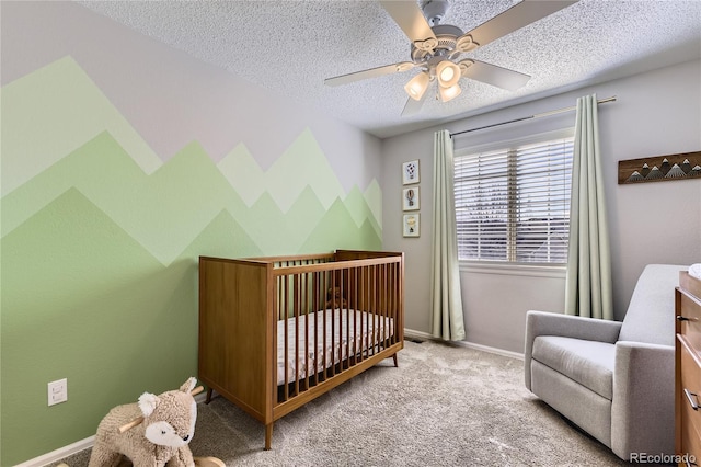 carpeted bedroom with ceiling fan, a textured ceiling, baseboards, and a crib