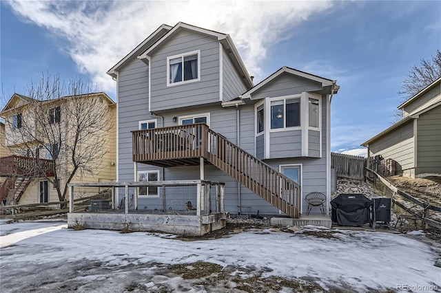 snow covered back of property featuring stairway, fence, and a wooden deck