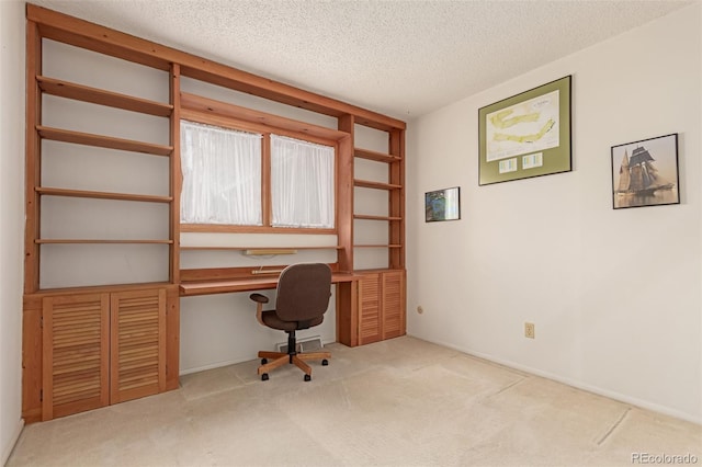 carpeted office space featuring a textured ceiling and built in desk