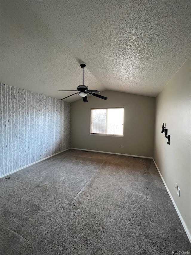 empty room featuring a textured ceiling, carpet, a ceiling fan, baseboards, and lofted ceiling