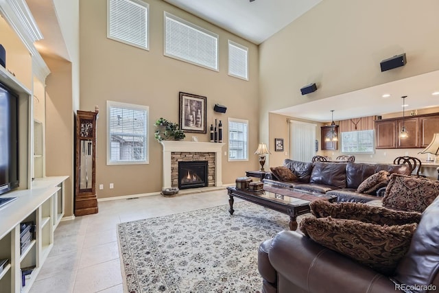 living area featuring light tile patterned floors, a stone fireplace, a towering ceiling, and baseboards