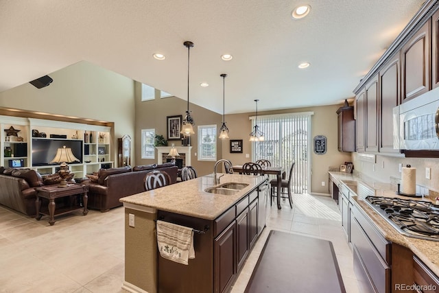 kitchen featuring a sink, open floor plan, dark brown cabinets, appliances with stainless steel finishes, and light stone countertops