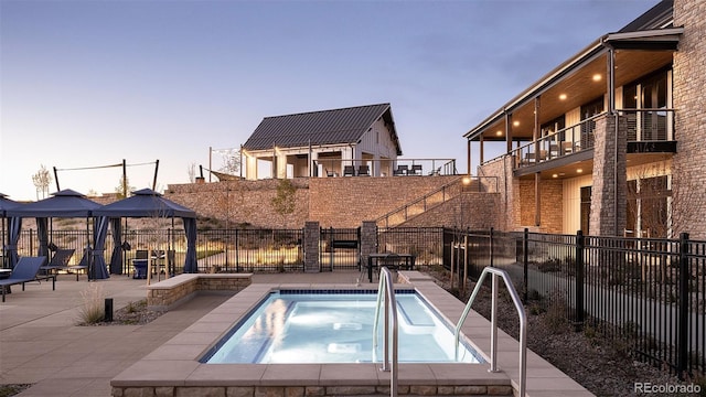 pool at dusk with a gazebo, an in ground hot tub, and a patio