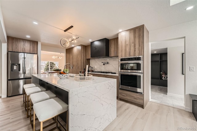 kitchen with appliances with stainless steel finishes, a kitchen breakfast bar, hanging light fixtures, a kitchen island with sink, and tasteful backsplash