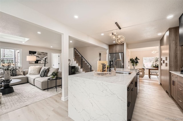 kitchen featuring a sink, light wood finished floors, an island with sink, dark brown cabinets, and recessed lighting