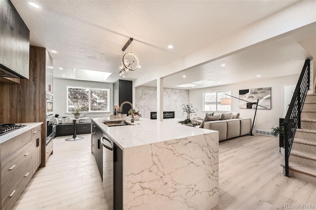 kitchen with a sink, light wood-style floors, dishwasher, a center island with sink, and a textured ceiling