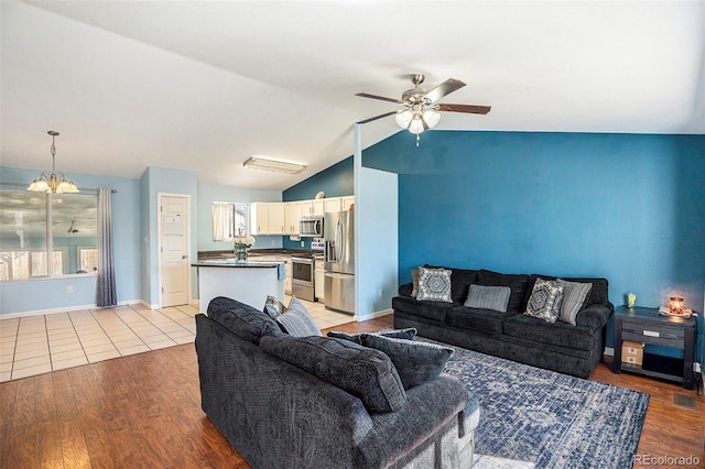 living area with lofted ceiling, ceiling fan with notable chandelier, visible vents, baseboards, and light wood-style floors