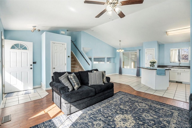 living room with light wood-type flooring, stairs, visible vents, and vaulted ceiling