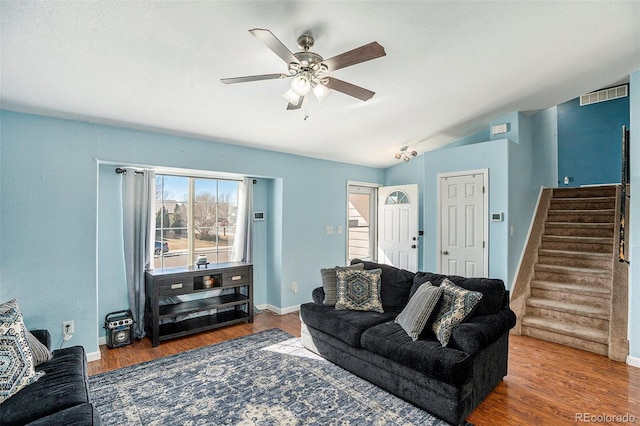 living area featuring lofted ceiling, visible vents, a ceiling fan, wood finished floors, and stairs