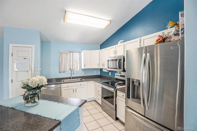 kitchen with dark countertops, lofted ceiling, appliances with stainless steel finishes, white cabinetry, and a sink