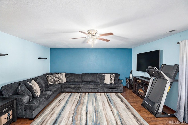 living room featuring a ceiling fan, visible vents, dark wood finished floors, and a textured ceiling