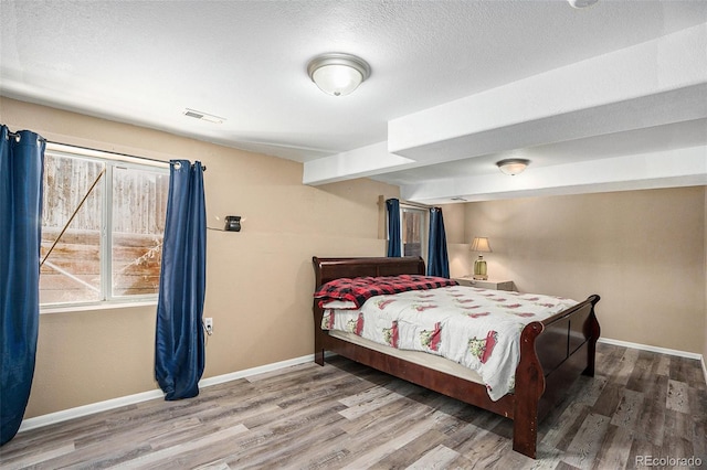 bedroom with visible vents, a textured ceiling, baseboards, and wood finished floors