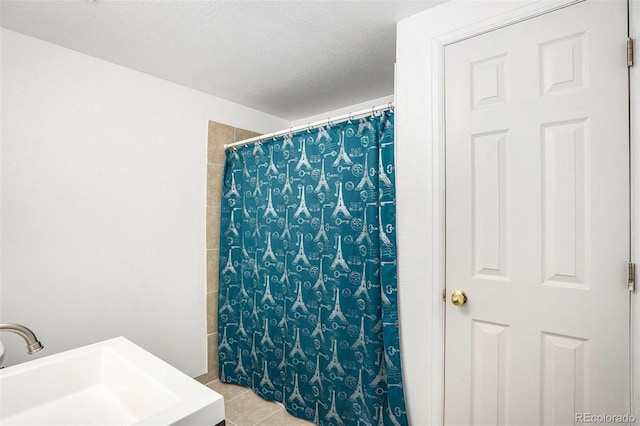 bathroom featuring a textured ceiling, curtained shower, tile patterned flooring, and a sink