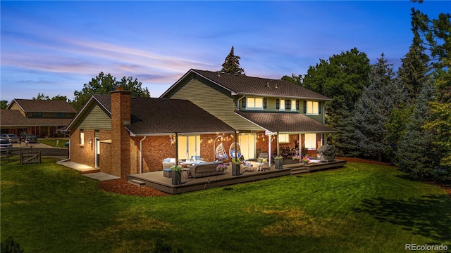 6795 E Kettle Ave, Centennial, CO 80112 - back of house at dusk with a chimney, a wooden deck, a lawn, an outdoor hangout area, and brick siding
