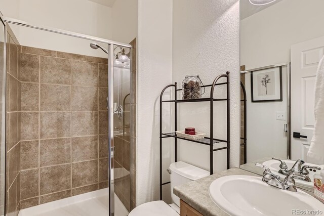 bathroom featuring a shower with shower door, toilet, and vanity