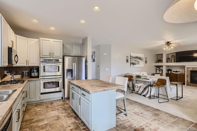 kitchen featuring a center island, a kitchen bar, white cabinetry, stainless steel appliances, and a fireplace