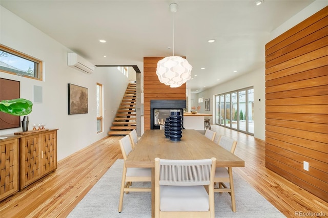 dining space with stairway, a multi sided fireplace, light wood-style floors, a wall unit AC, and recessed lighting
