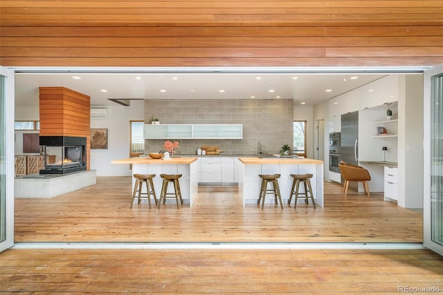 kitchen featuring wooden counters, a multi sided fireplace, modern cabinets, a kitchen island, and white cabinetry