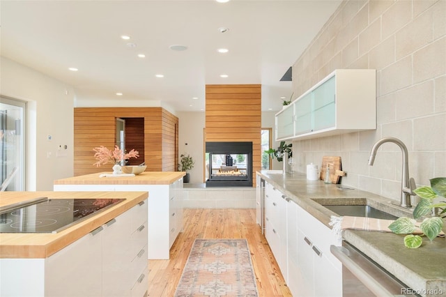 kitchen with black electric cooktop, wooden counters, white cabinetry, and a sink