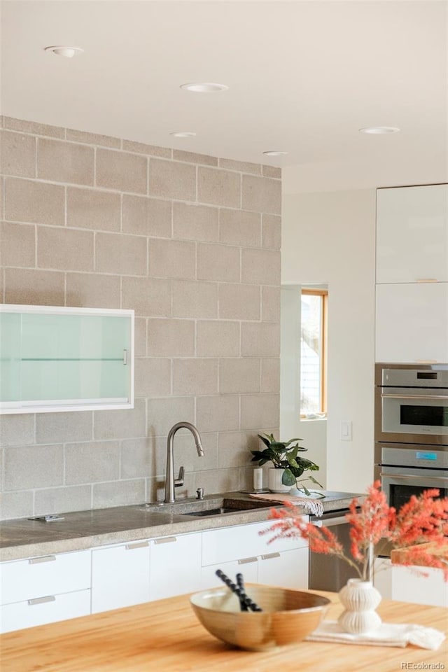 kitchen featuring white cabinets, backsplash, stainless steel double oven, and a sink