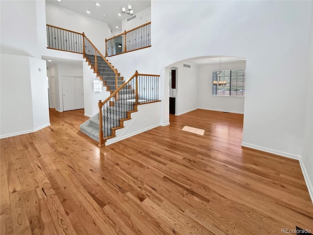 2180 Trailblazer Way, Castle Rock, CO 80109 - unfurnished living room with a chandelier, arched walkways, stairs, light wood finished floors, and a towering ceiling