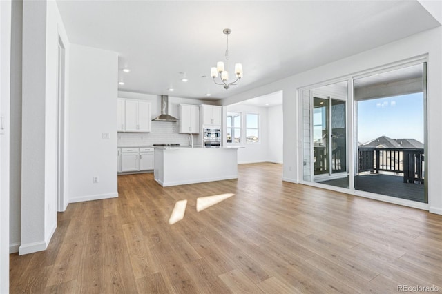 kitchen featuring pendant lighting, wall chimney range hood, backsplash, white cabinets, and light wood-type flooring