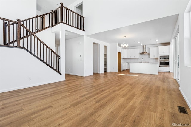 unfurnished living room with sink, a chandelier, light hardwood / wood-style floors, and a high ceiling