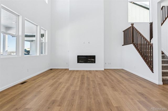 unfurnished living room featuring a towering ceiling and light wood-type flooring