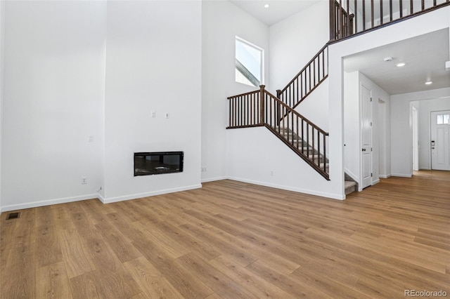 unfurnished living room with heating unit, light wood-type flooring, and a high ceiling