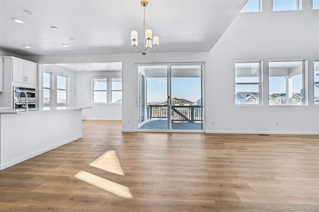 unfurnished living room featuring an inviting chandelier and light hardwood / wood-style floors