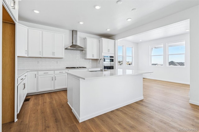 kitchen with sink, white cabinets, wall chimney exhaust hood, and a center island with sink