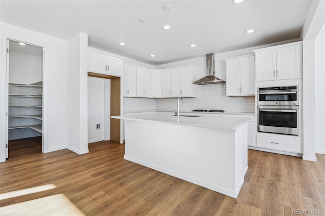 kitchen with white cabinetry, wall chimney exhaust hood, and a kitchen island with sink