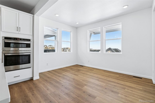 kitchen featuring double oven, light hardwood / wood-style flooring, and white cabinets