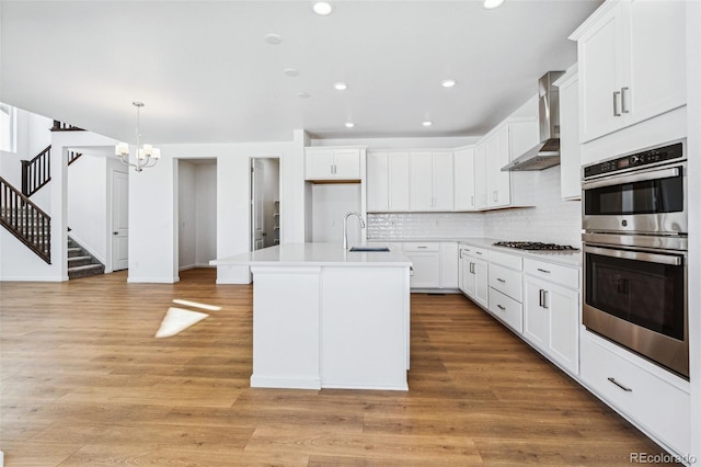 kitchen featuring appliances with stainless steel finishes, white cabinetry, sink, a kitchen island with sink, and wall chimney exhaust hood