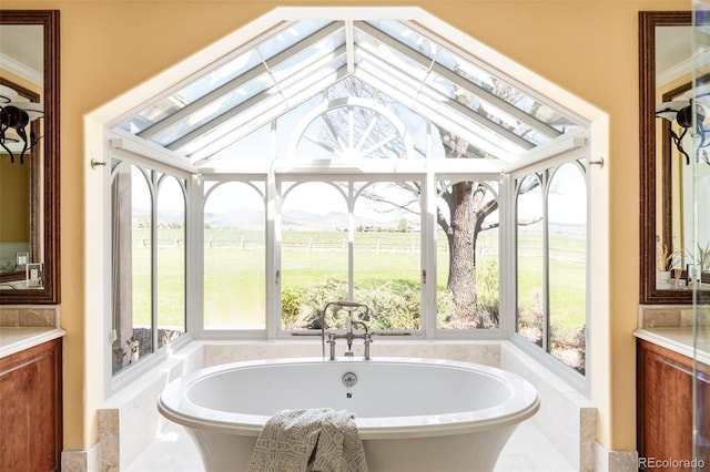 full bath featuring plenty of natural light, a view of countryside, a soaking tub, vaulted ceiling, and vanity