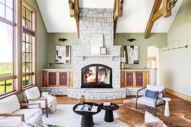 living area with high vaulted ceiling, wood finished floors, a stone fireplace, beam ceiling, and healthy amount of natural light