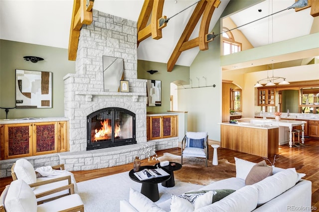 living room featuring high vaulted ceiling, wood finished floors, a stone fireplace, and beam ceiling