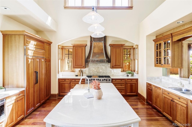 kitchen with custom exhaust hood, a sink, high end stainless steel range, light countertops, and a center island with sink