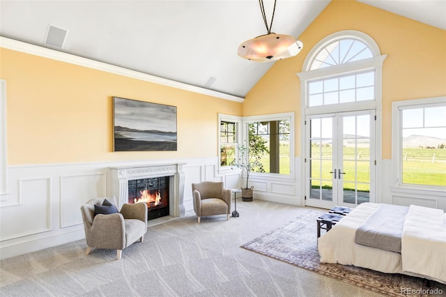 carpeted bedroom with access to exterior, a decorative wall, a lit fireplace, wainscoting, and french doors