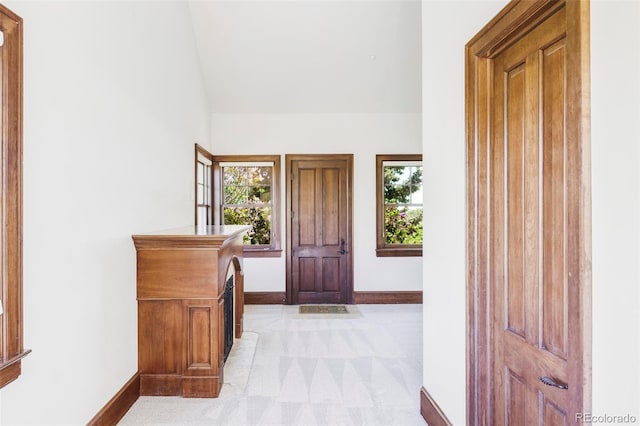 entrance foyer with baseboards, vaulted ceiling, light carpet, and plenty of natural light
