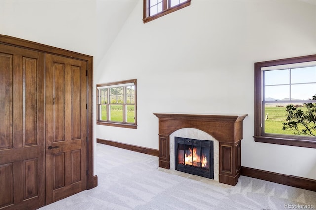 living area featuring a high ceiling, baseboards, light carpet, and a fireplace with flush hearth